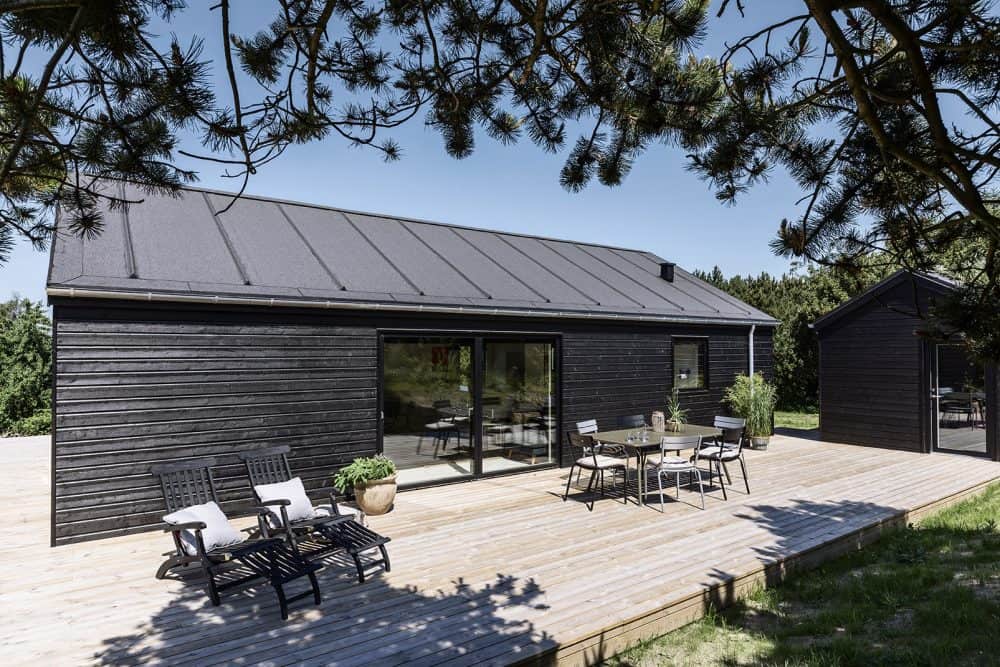 Rummelig træterrasse foran sommerhus med sort træ beklædning