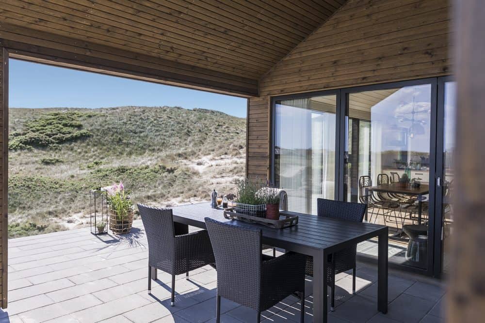 Sommerhus beliggende i klitter med havemøbler under overdækket terrasse