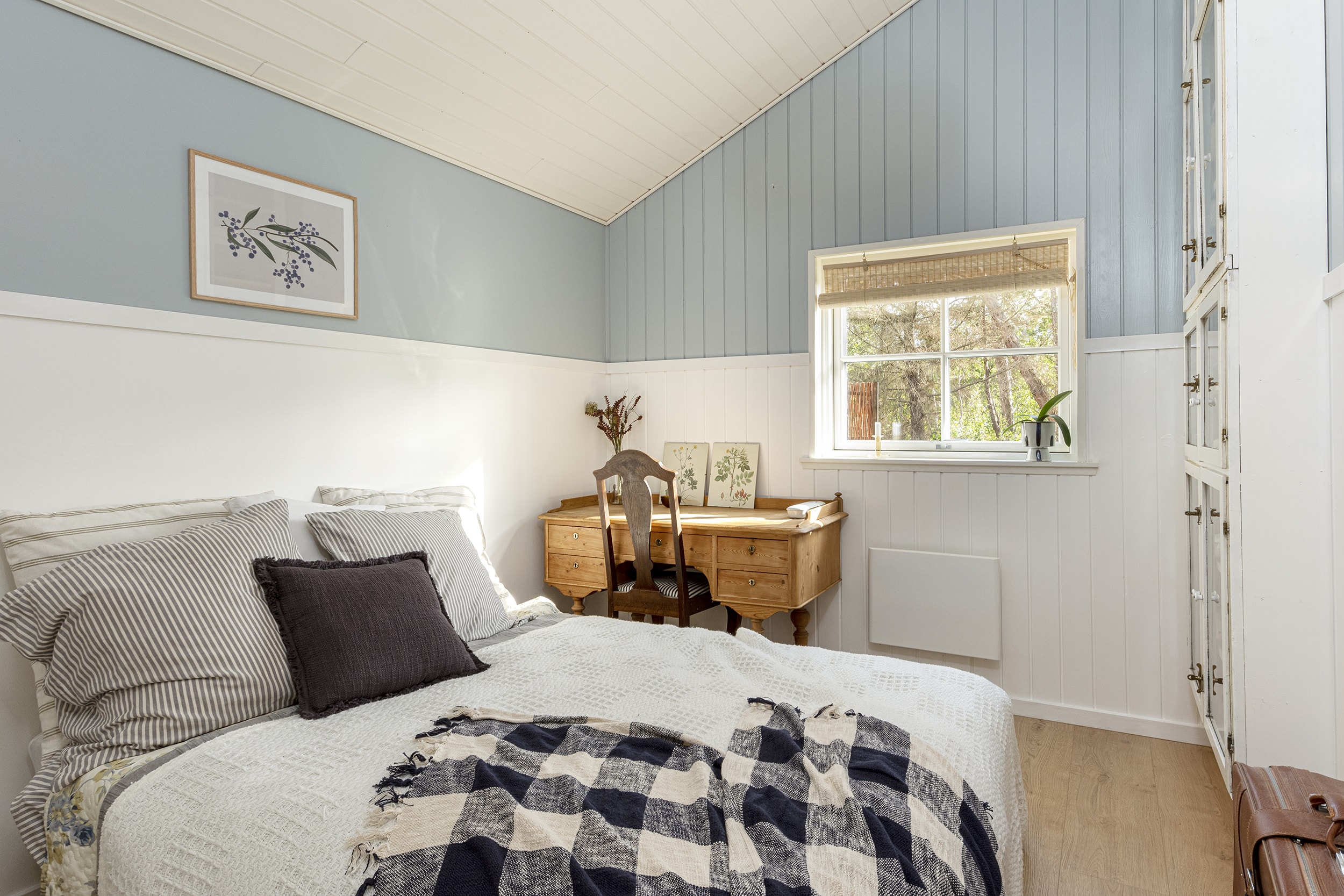 Soveværelse med seng, hvide og blå vægge og lille vindue