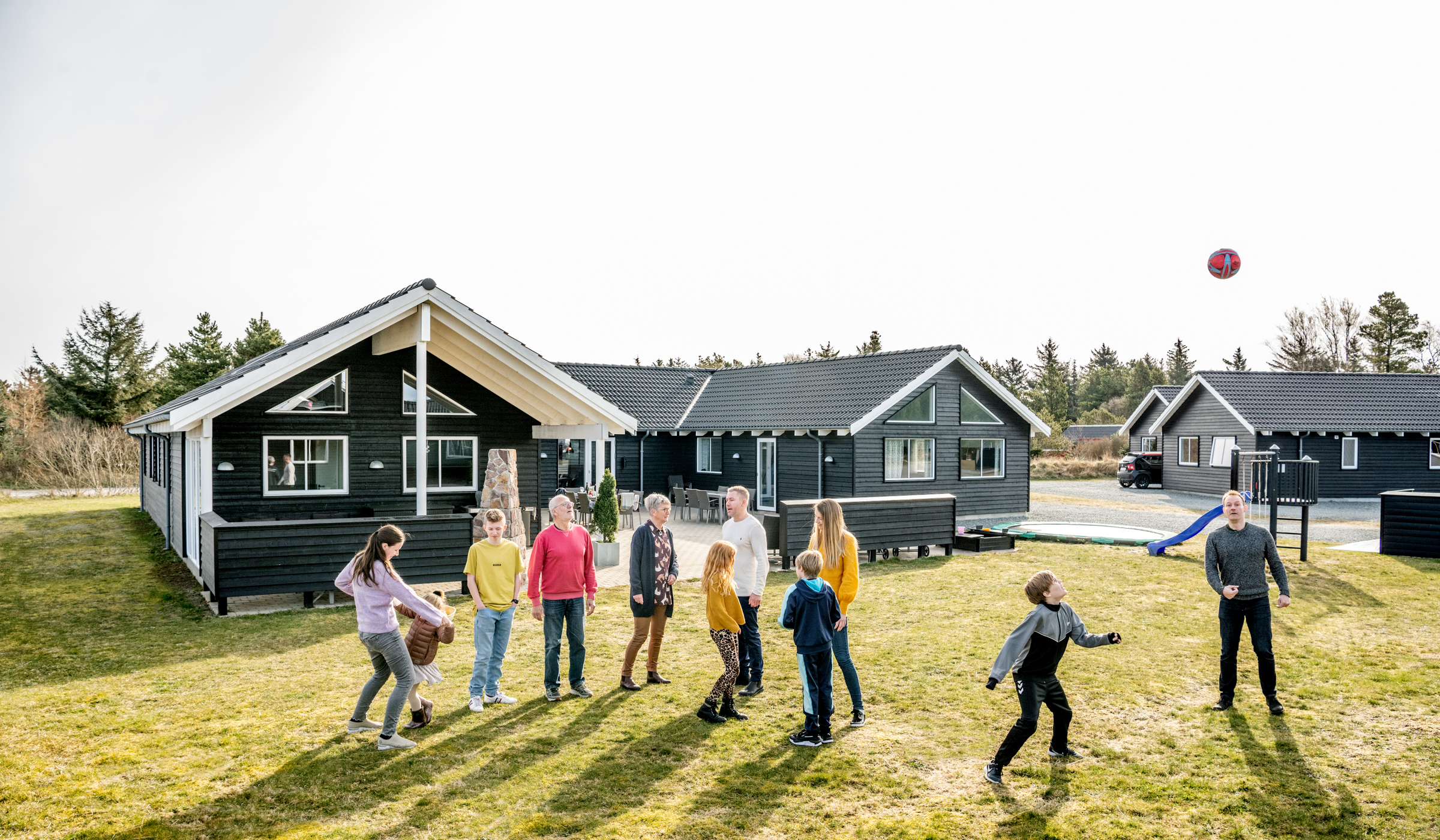 Familie leger og spiller fodbold på græsplæne foran sommerhus