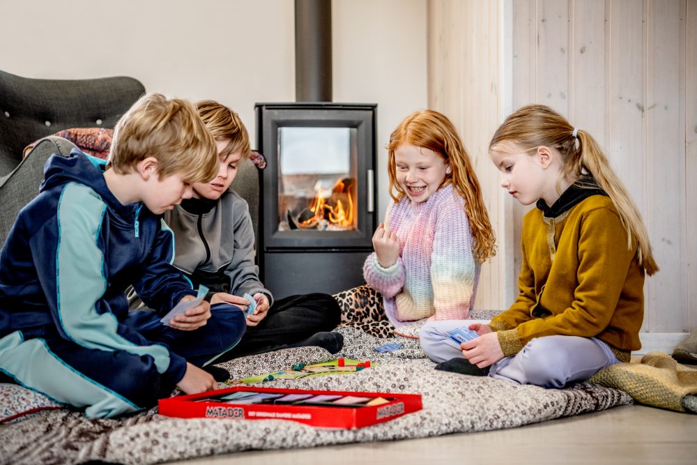 Børn spiller spil foran tændt brændeovn
