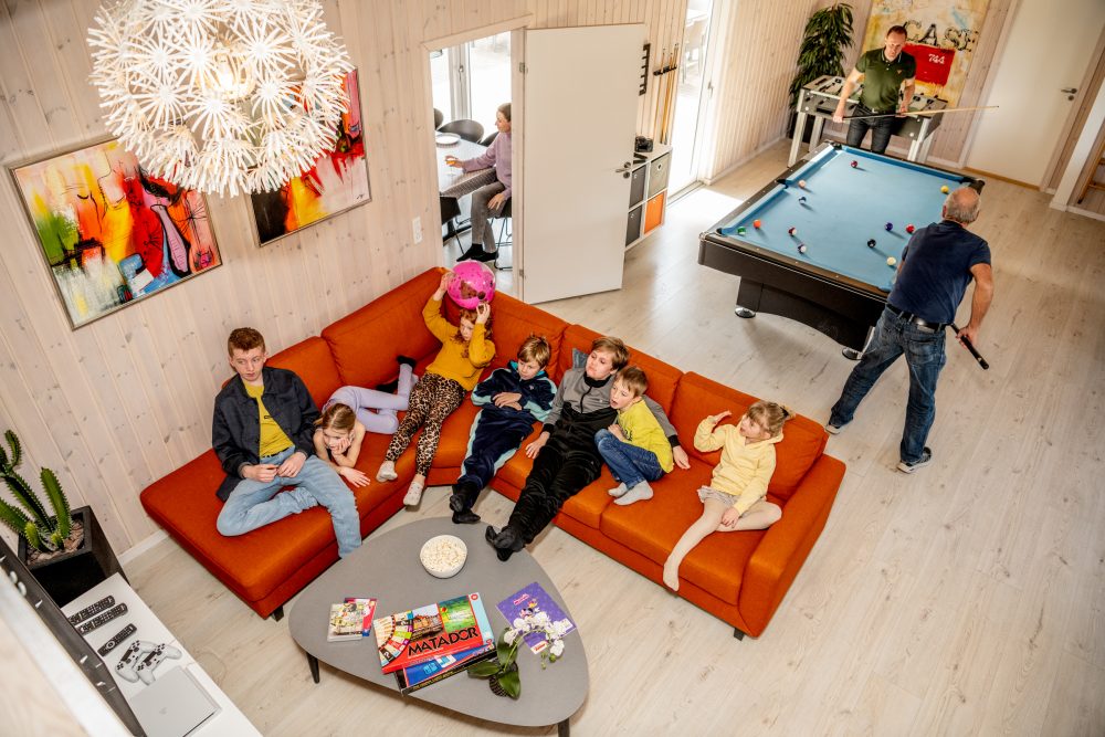 Aktivitetsrum i sommerhus med børn der ser tv og mænd der spiller billard