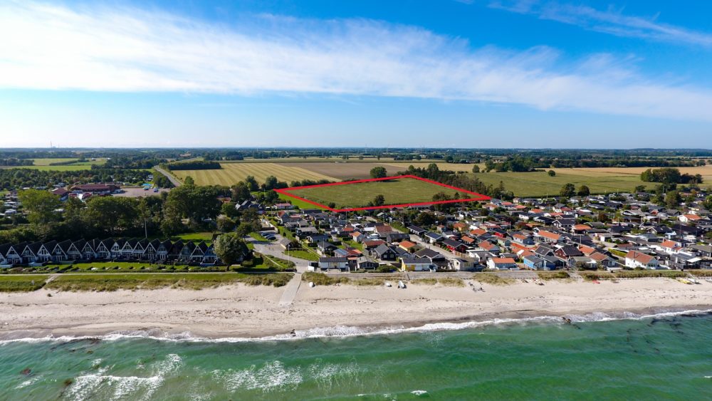 Dronefoto af sommerhusgrunde med hav, by og mark