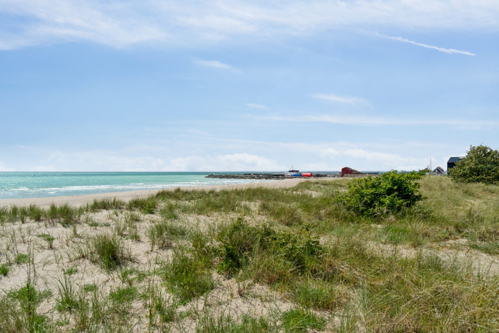 Skøn sandstrand med blåt vand nær havn